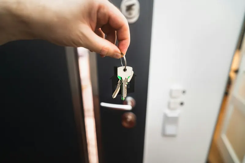 Personne tenant un trousseau de clés devant une porte d'entrée